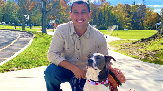 A brown and white dog sits outside next to a man kneeling beside him