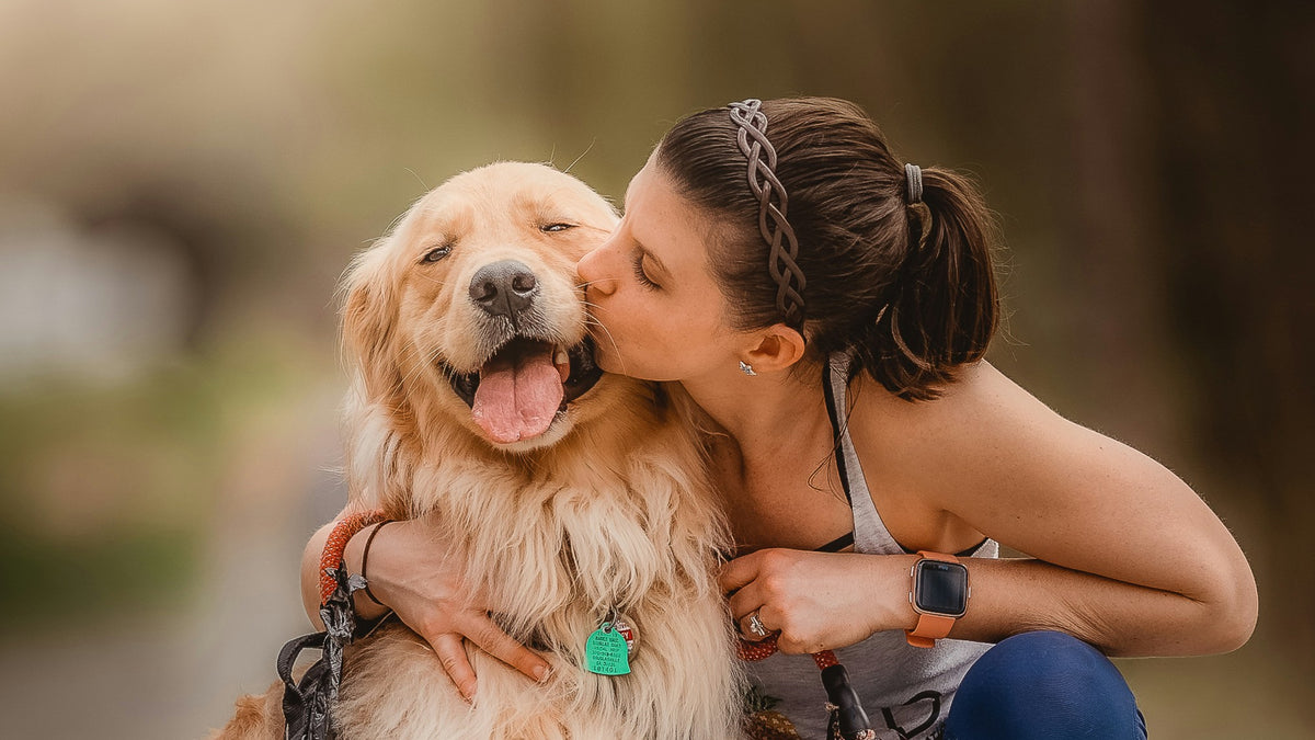 A girl with brown hair kisses a golden retreiver dog on its cheek