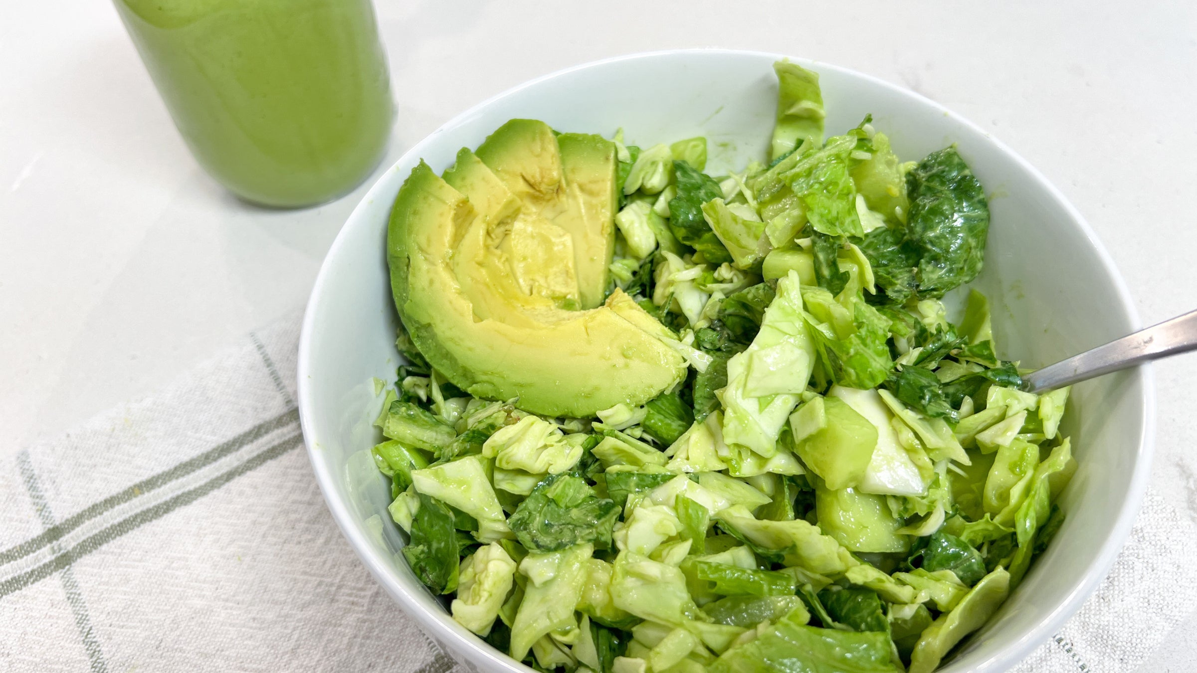 A green salad with avocado in a white bowl