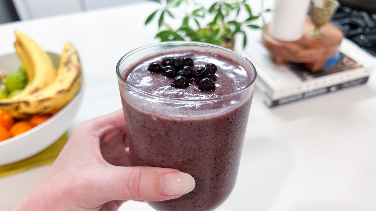 A hand holds a clear glass filled with a purple immune boosting smoothie