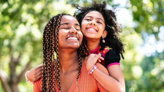 A mom and her daughter hug and smile with a backdrop of trees