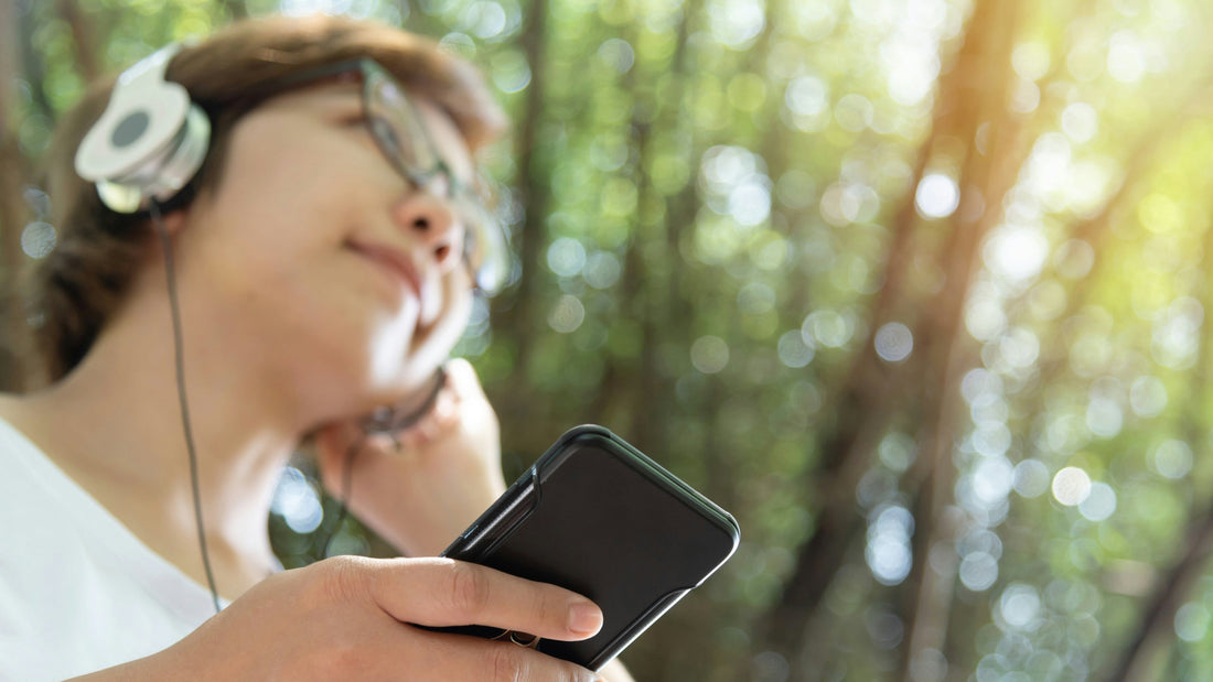A person listening to their headphones outside with trees in the background