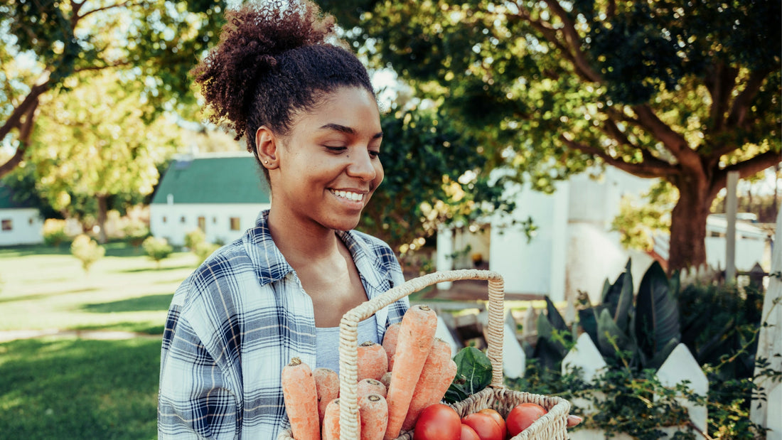 A woman with her hair up carries a basket of carrots and apples