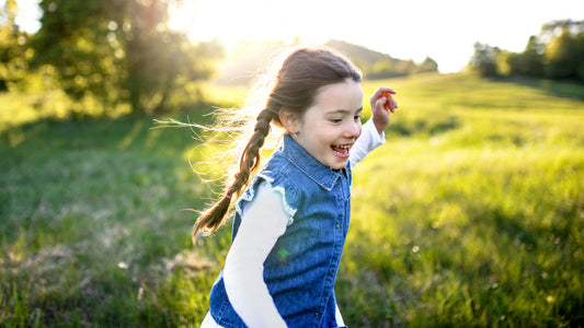 A young girl with braids runs through a green field with the sunlight behind her