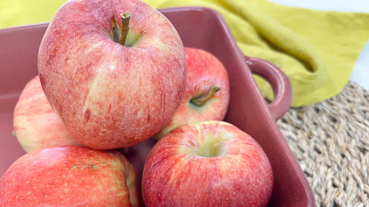 Several red apples in red pan with a green towel behind