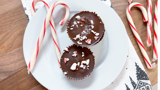 Two chocolate peppermint patties sit on a white plate with candy canes in the frame