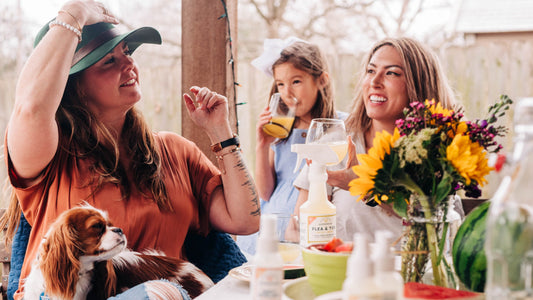 Two women a child and a dog enjoy time on the patio outdoors with a boquet of flowers on the table in front