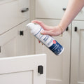 A person’s hand holds Wondercide Ant & Roach for Home + Kitchen spray, aiming at an open white kitchen cabinet. This plant-powered spray kills ants and roaches effectively without harsh chemicals and is safe around pets.