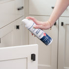 A person’s hand holds Wondercide Ant & Roach for Home + Kitchen spray, aiming at an open white kitchen cabinet. This plant-powered spray kills ants and roaches effectively without harsh chemicals and is safe around pets.