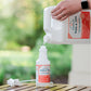 Someone pours Wondercide 128 oz. Peppermint Flea & Tick Spray for Pets + Home with Natural Essential Oils into a smaller spray bottle on a wooden surface, with a green outdoor background.