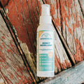 A white spray bottle of Wondercide Cedarwood Insect Repellent for Family sits on weathered, peeling red and gray wood.