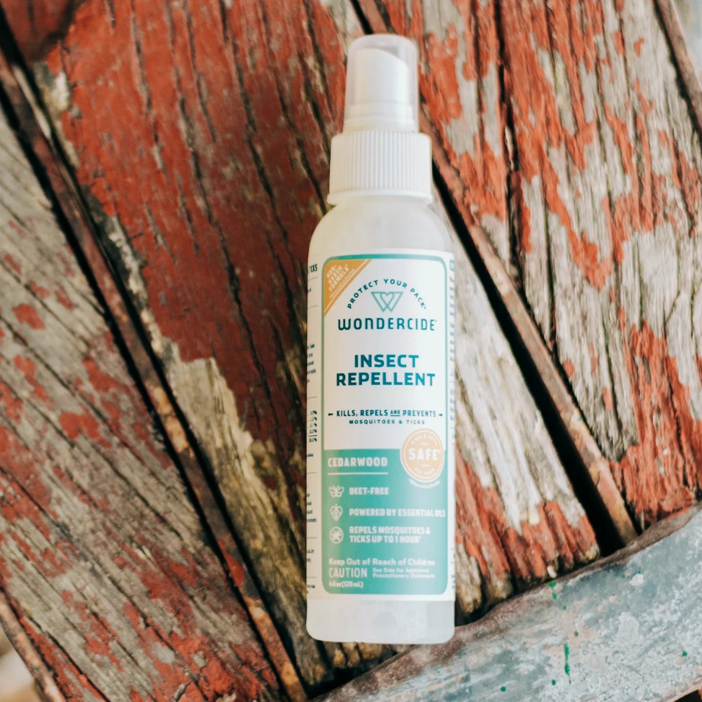A bottle of Wondercide Cedarwood Insect Repellent for Family with Natural Essential Oils sits on a weathered red and gray wooden surface. Its label highlights DEET-free, plant-powered protection against insects.