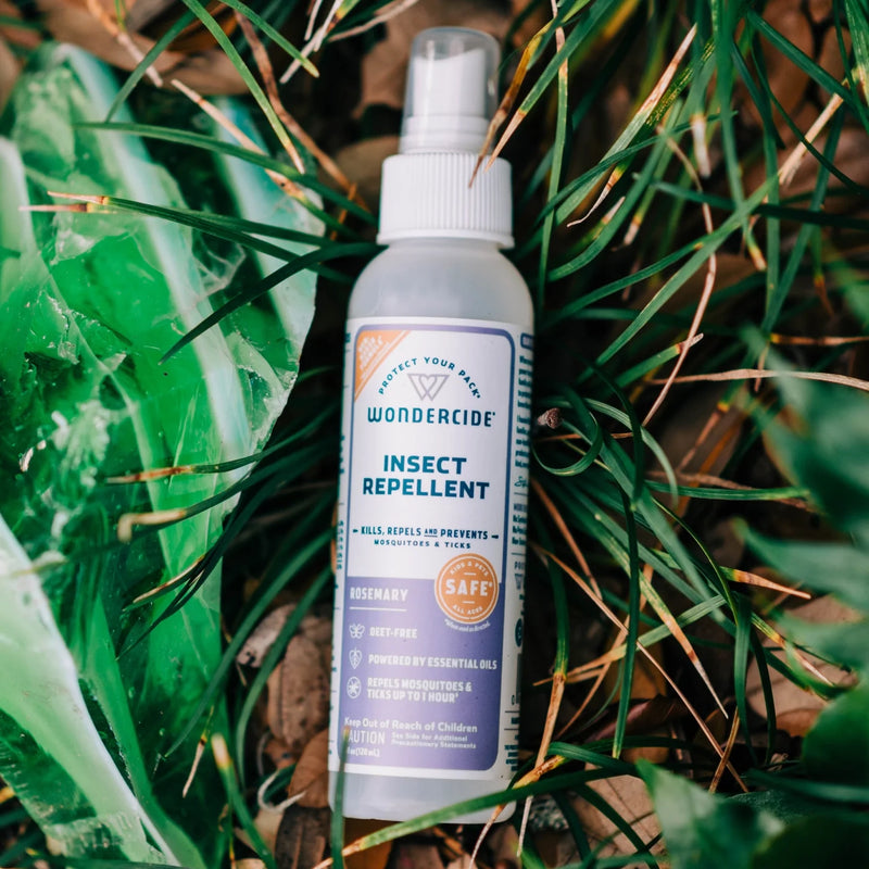 A bottle of Wondercide Rosemary Insect Repellent for Family sits on grass and leaves, its label showing it's DEET-free, powered by essential oils, and repels ticks and mosquitoes.