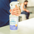 A hand holds a 128 oz. Wondercide Rosemary Indoor Pest Control bottle on a kitchen counter, with an out-of-focus person in the background.