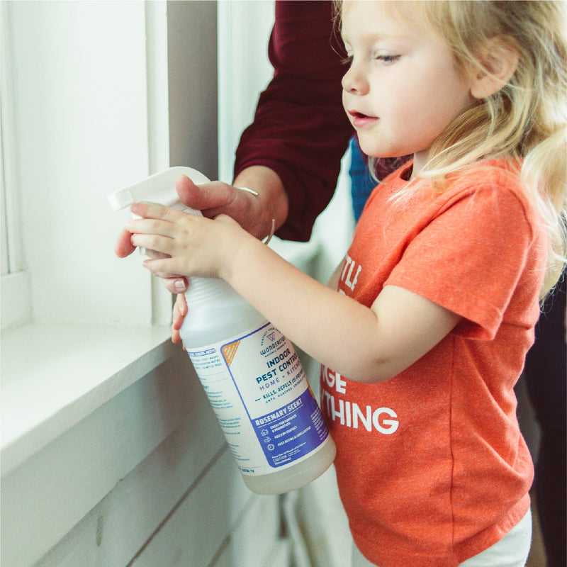 A young child, guided by an adult’s hand, holds Wondercide’s 128 oz. Rosemary Indoor Pest Control near a window.