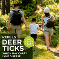 A family of three hiking on a forest path, viewed from behind, with a dark green text banner in the lower left that reads 'REPELS DEER TICKS WHICH MAY CARRY LYME DISEASE' alongside a green tick icon.