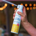 A hand sprays Wondercide Wasp & Hornet for Porch + Patio outdoors, with blurred lights in the background—the perfect solution for killing wasps and yellow jackets.